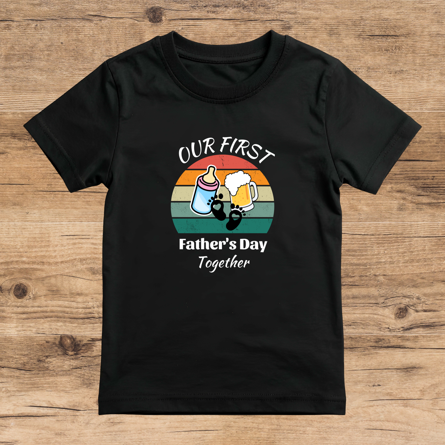 Black t-shirt with 'Our First Father's Day Together' graphic on a wooden surface