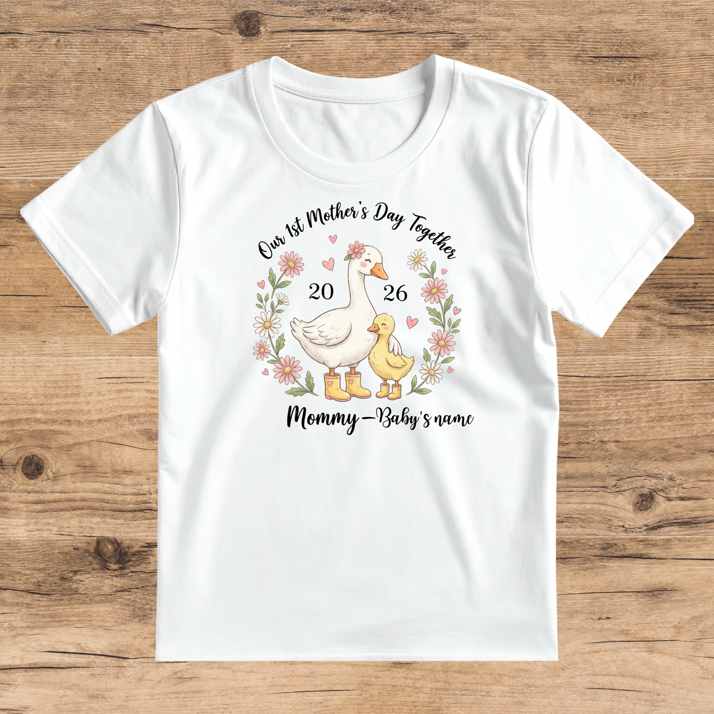 White t-shirt with a graphic of a mother duck and duckling, flowers, and text on a wooden surface.