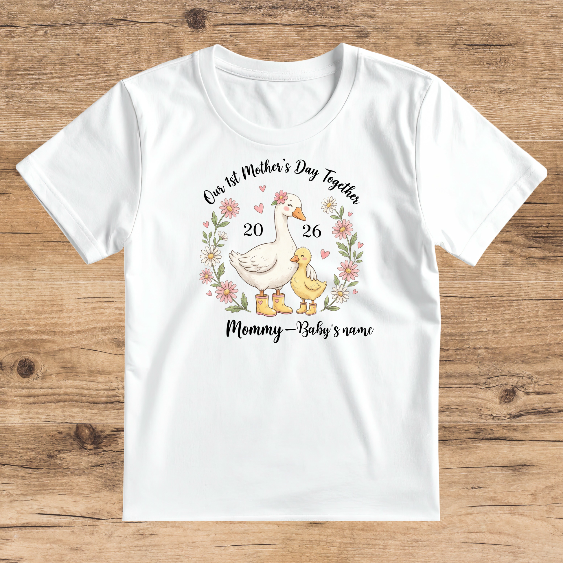 White t-shirt with a graphic of a mother duck and duckling, flowers, and text on a wooden surface.