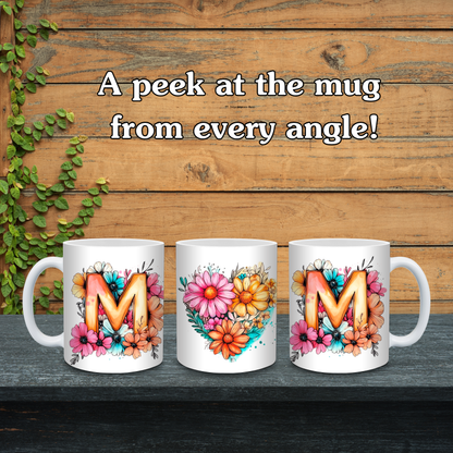 Three white mugs with floral designs and letters 'M' on a wooden background