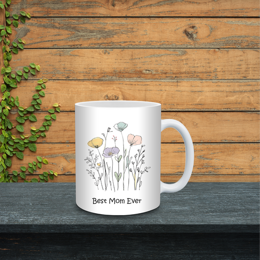 White mug with floral design and 'Best Mom Ever' text on a wooden surface with greenery.