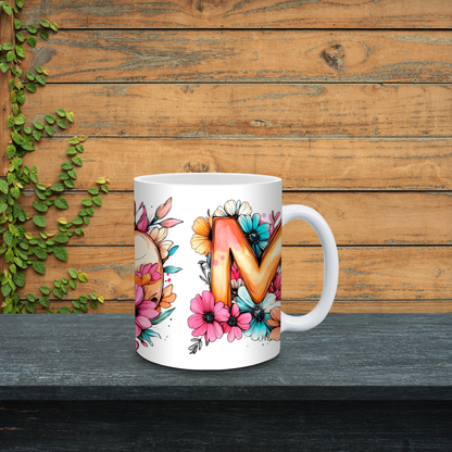 White mug with floral design and letter 'M' on a wooden background