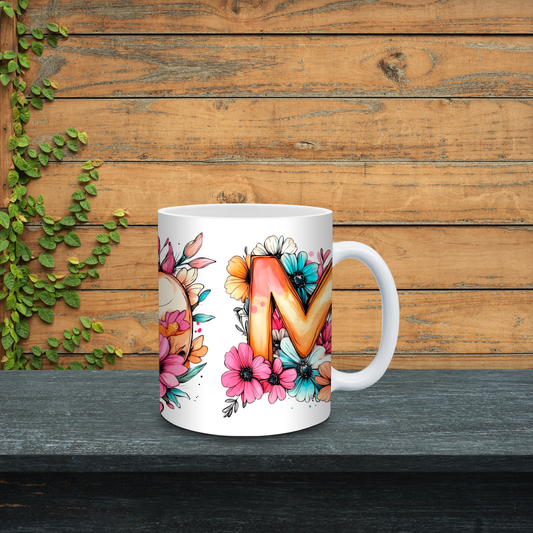White mug with floral design and letter 'M' on a wooden background