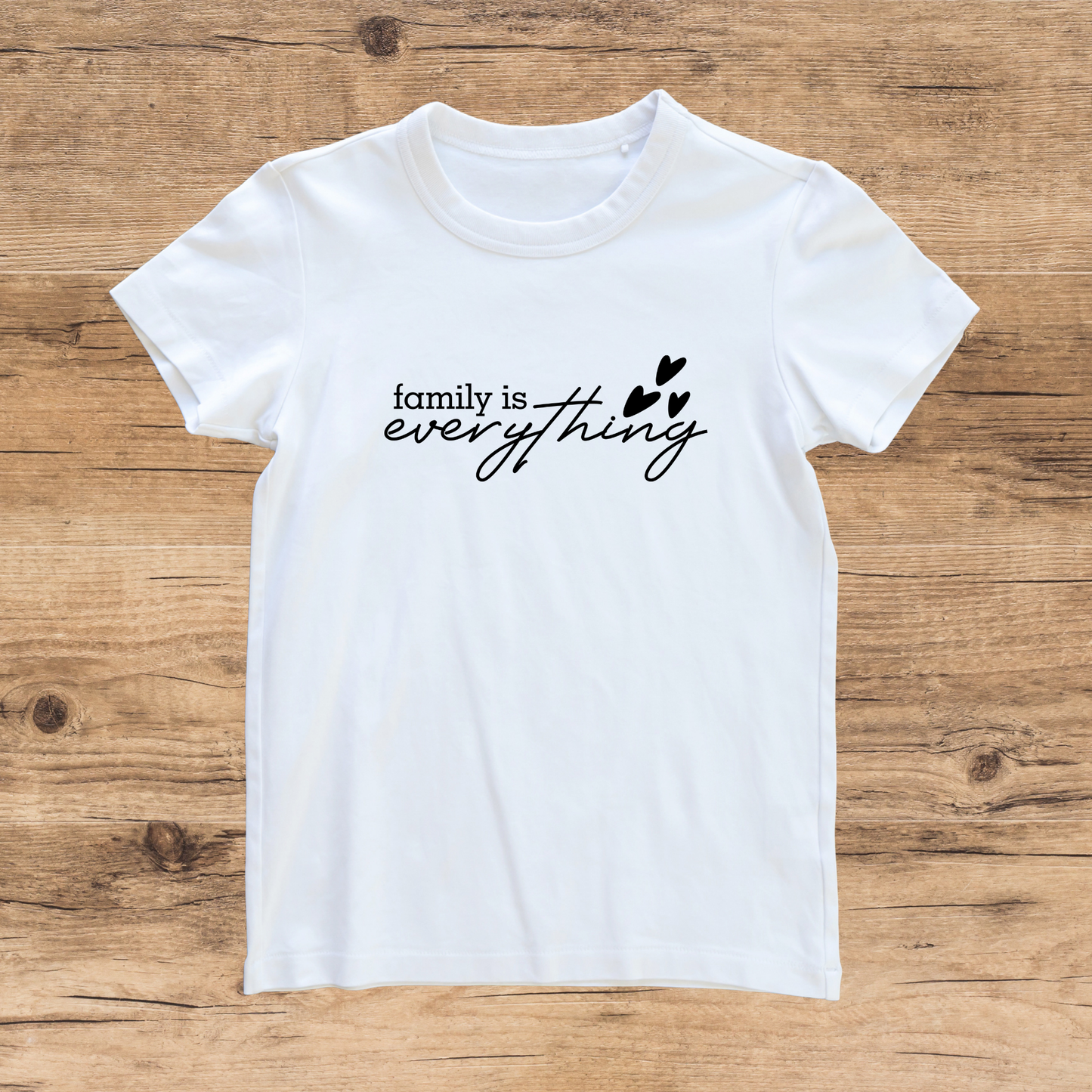 White t-shirt with 'family is everything' text on a wooden surface