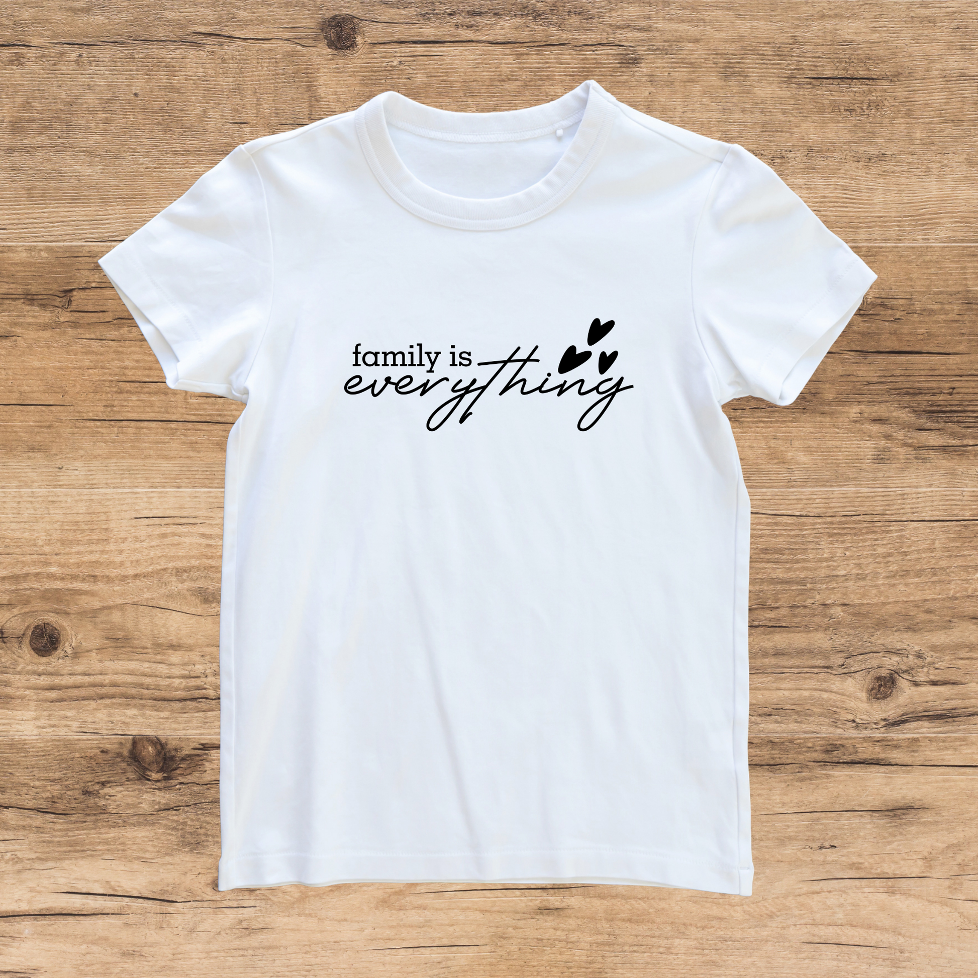 White t-shirt with 'family is everything' text on a wooden surface