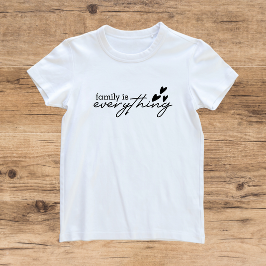 White t-shirt with 'family is everything' text on a wooden surface