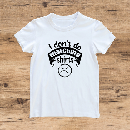 White t-shirt with black text and an angry face emoji on a wooden surface