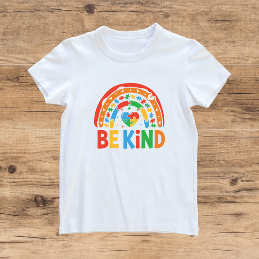 White t-shirt with a colorful rainbow and 'BE KIND' text on a wooden surface
