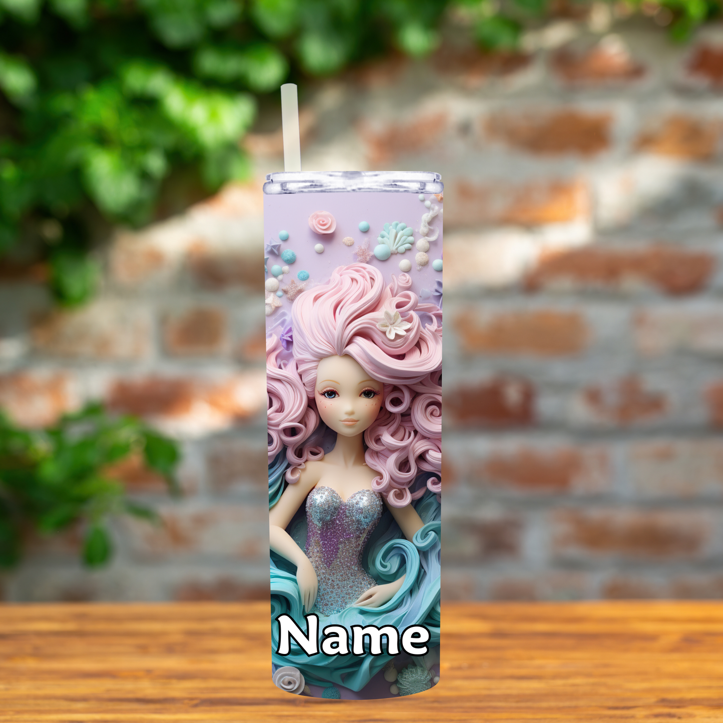 Tumbler with a decorative design of a mermaid and pink hair on a wooden surface with a brick wall background.