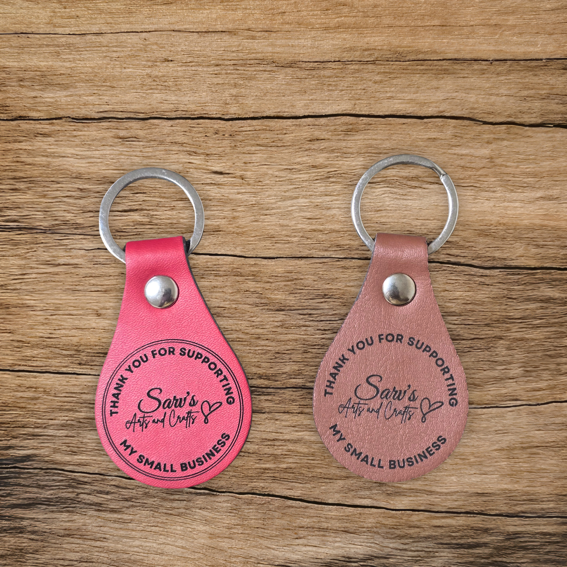 Two pink leather keychains with engraved text on a wooden surface