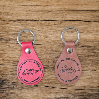 Two pink leather keychains with engraved text on a wooden surface