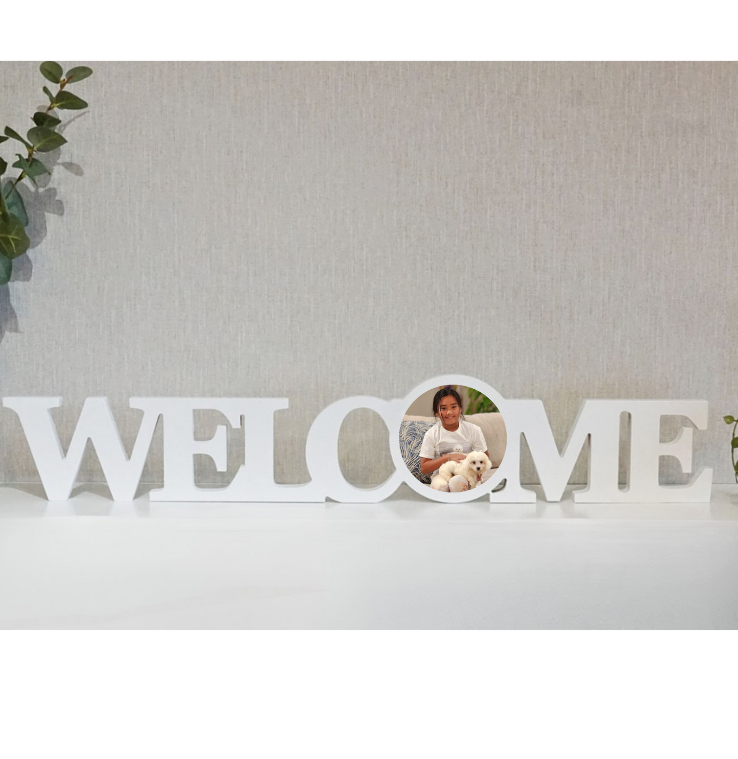 White 'WELCOME' sign with a mirror reflecting a person holding a dog against a light gray wall.