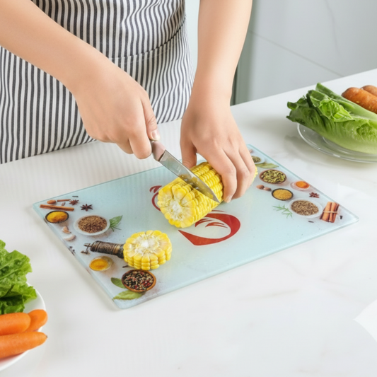 Person cutting corn on a decorative cutting board with kitchen items around