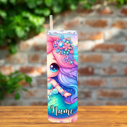 Colorful mermaid-themed tumbler with a straw on a wooden surface and brick wall background.