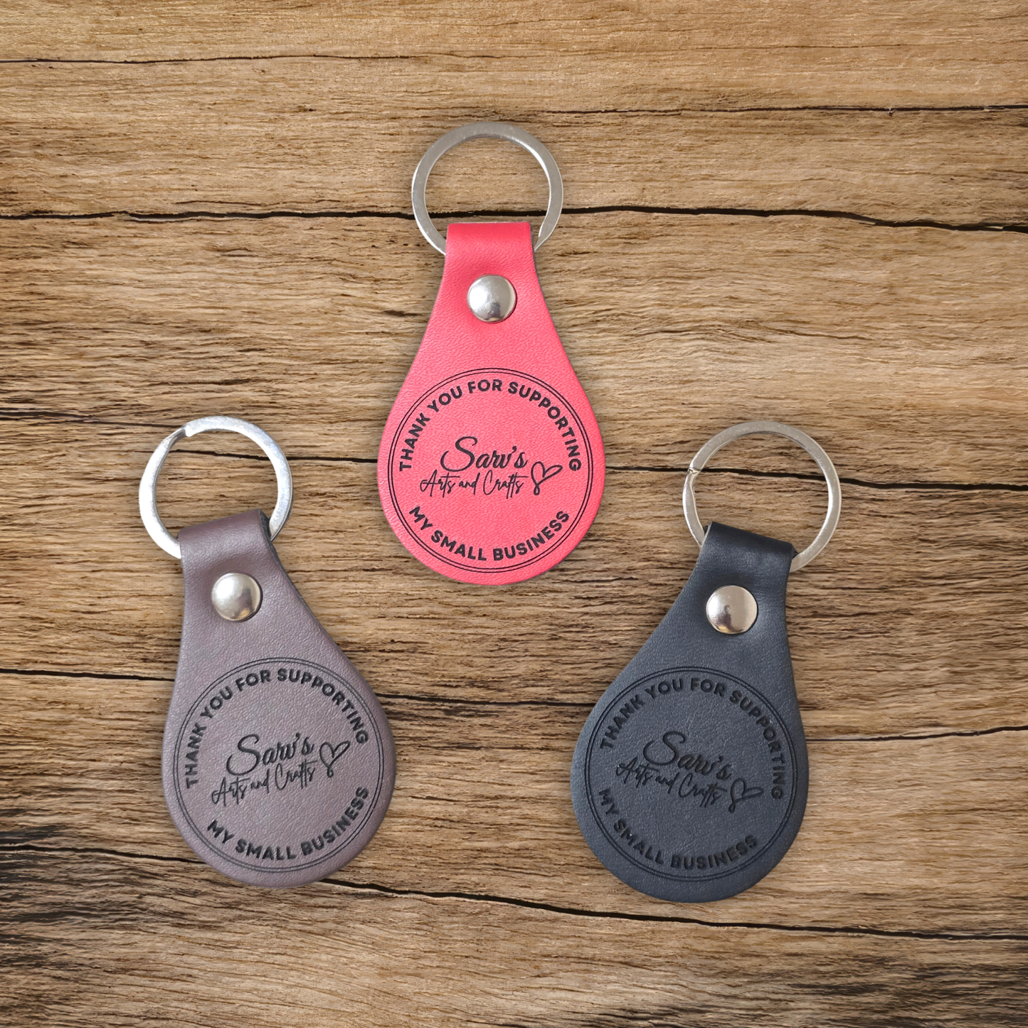 Three leather keychains on a wooden surface, featuring 'Sara's Arts and Crafts' branding.