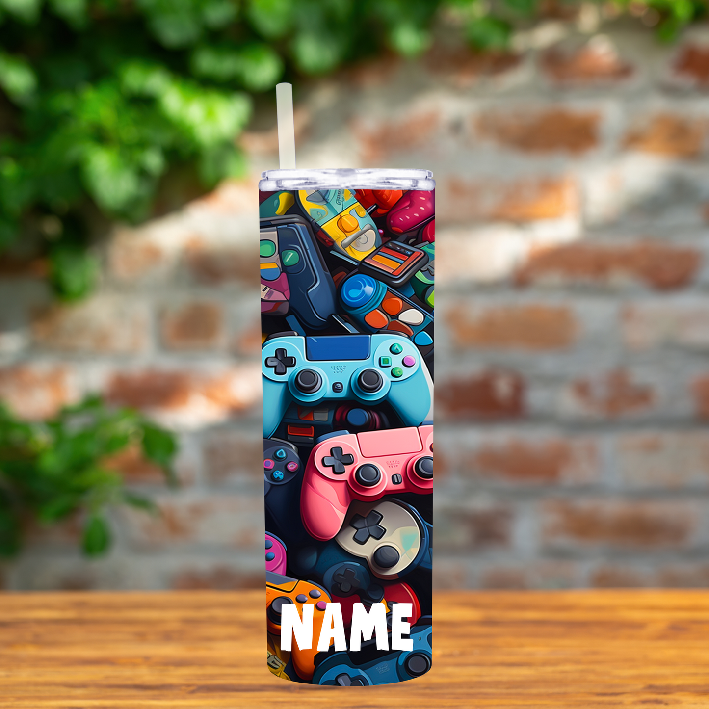 Tumbler with colorful game controller design on a wooden surface with a brick wall background