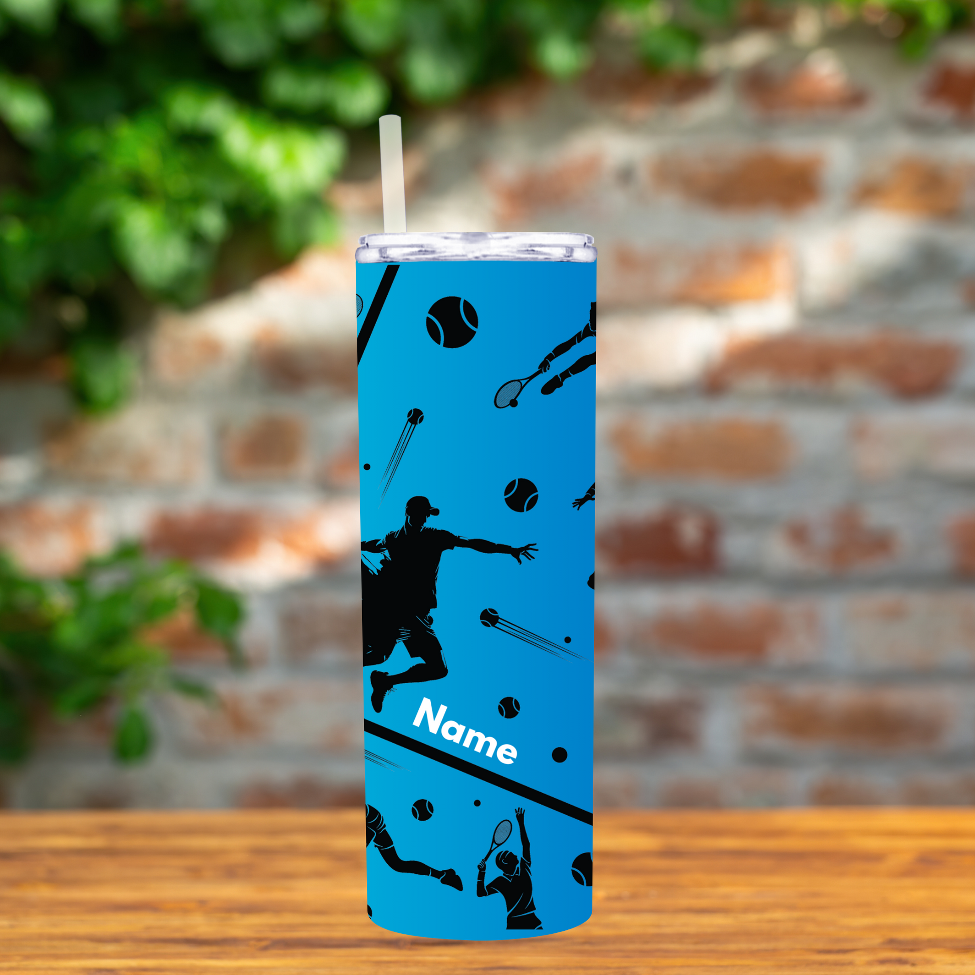 Blue tumbler with tennis-themed design on a wooden surface with a brick wall background