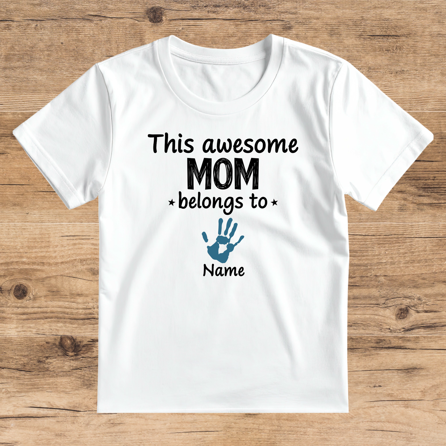 White t-shirt with text 'This awesome mom belongs to *Name*' on a wooden surface