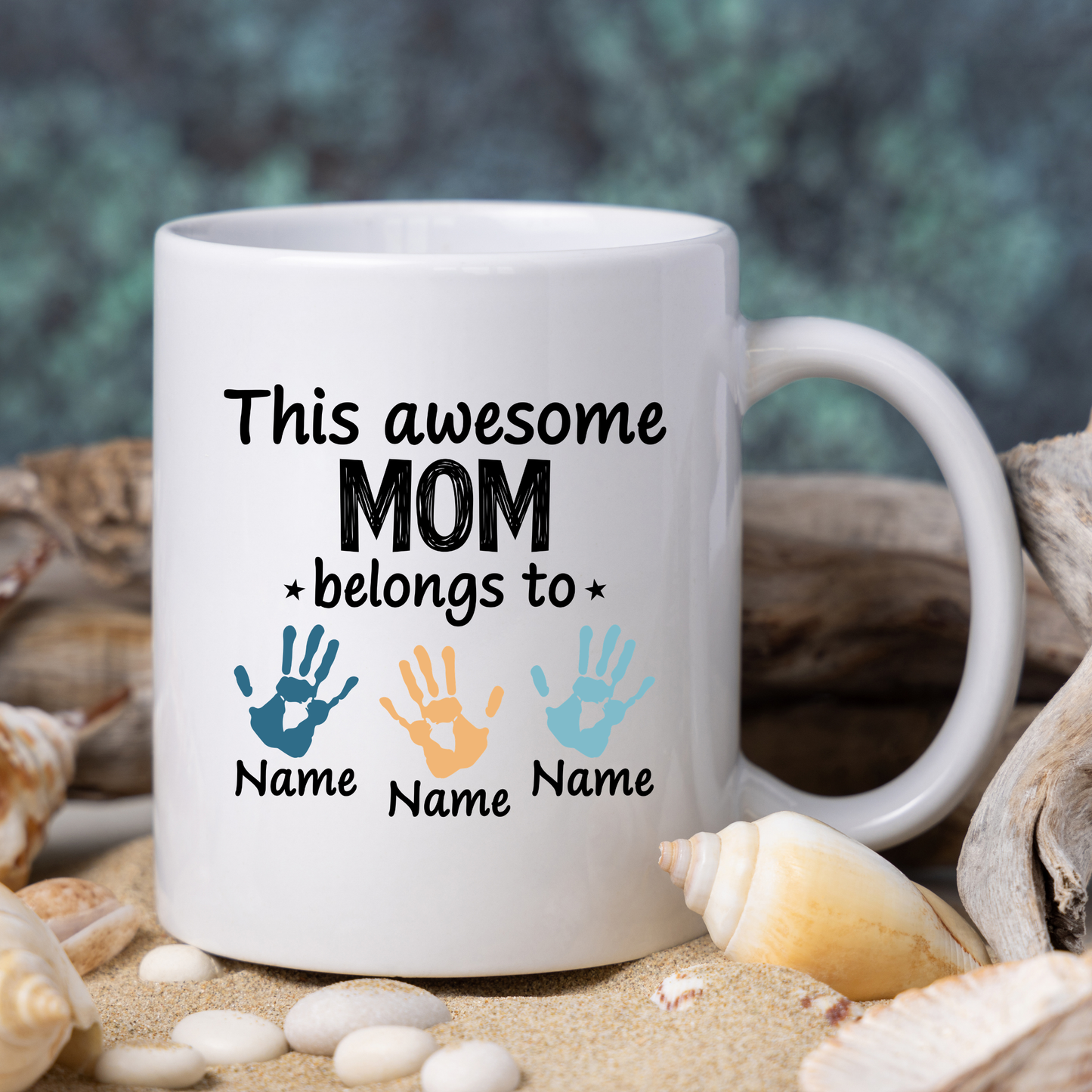 White mug with 'This awesome mom belongs to' text and handprints on a beach background