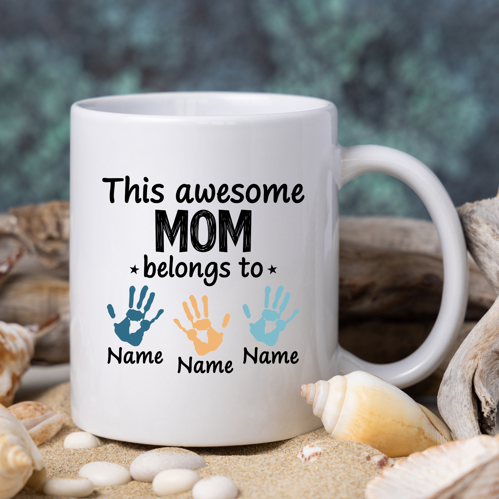 White mug with 'This awesome mom belongs to' text and handprints on a beach background