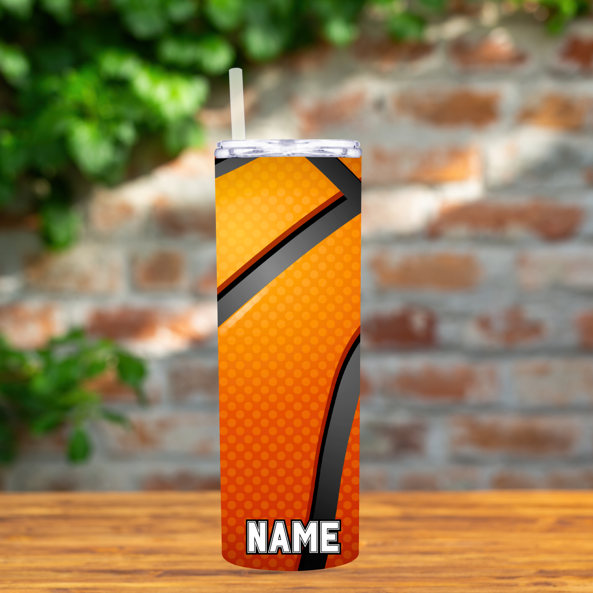 Orange tumbler with basketball design on a wooden surface with a blurred brick wall background