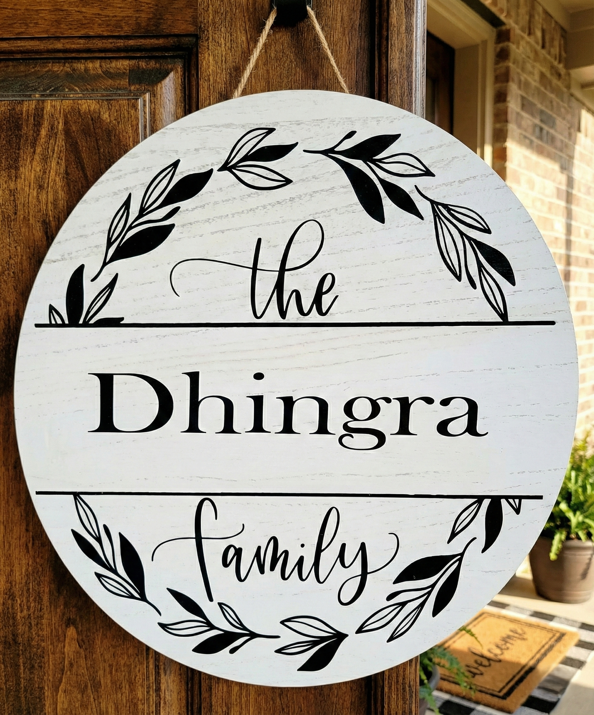 Round wooden sign with 'the Dhingra Family' text and leaf designs, hanging on a door.