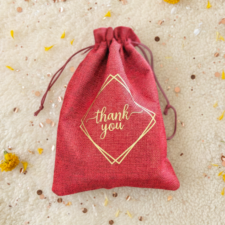 Red drawstring bag with 'thank you' text on a textured beige background