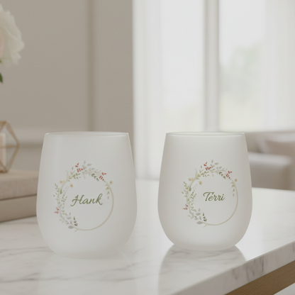 Two white wine glasses with floral designs and names on a marble surface.