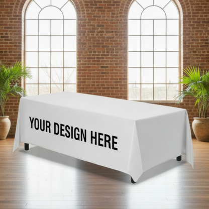 White tablecloth with 'YOUR DESIGN HERE' text in a room with brick walls and large windows.