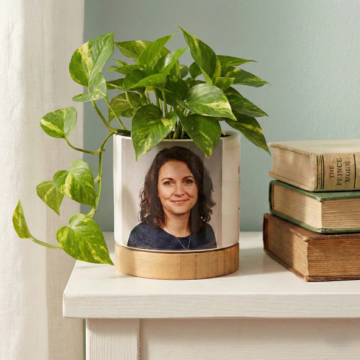 Decorative planter with a portrait on a shelf with books and a plant.