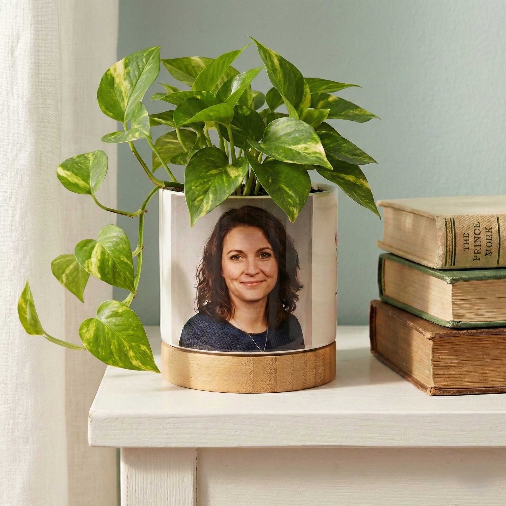 Decorative planter with a portrait on a shelf with books and a plant.