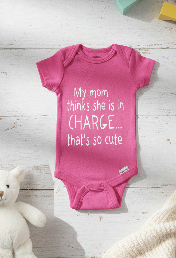 Pink baby onesie with text on a wooden surface with a teddy bear.