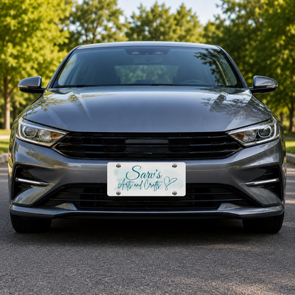 A front-facing gray sedan parked outdoors on asphalt with trees in the background. The front license plate reads 'Sari's Auto and Charities' in teal script with a heart.