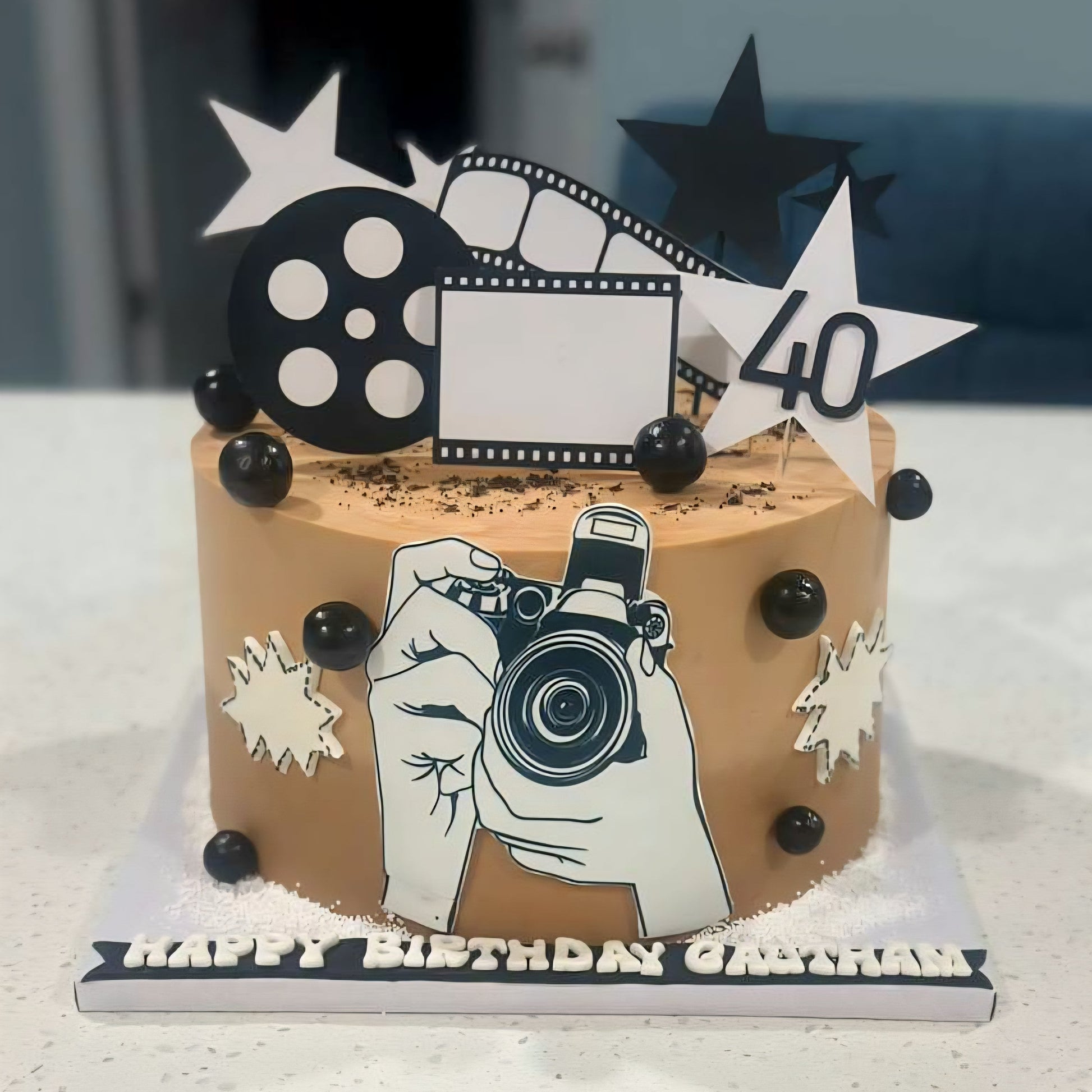 Birthday cake with camera-themed decorations and 'Happy Birthday' topper on a white surface.