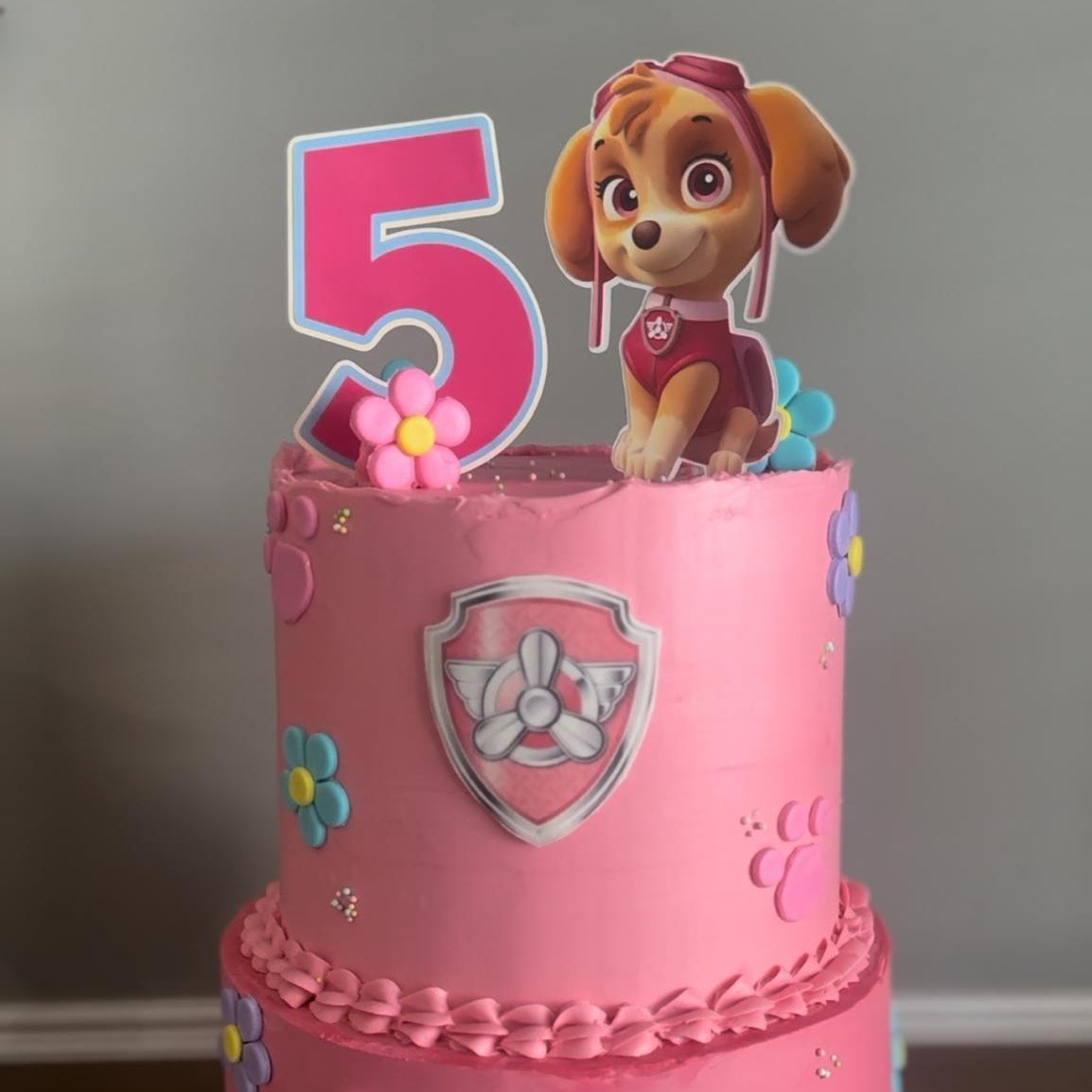 Pink birthday cake with a number 5 topper and character on a white surface.