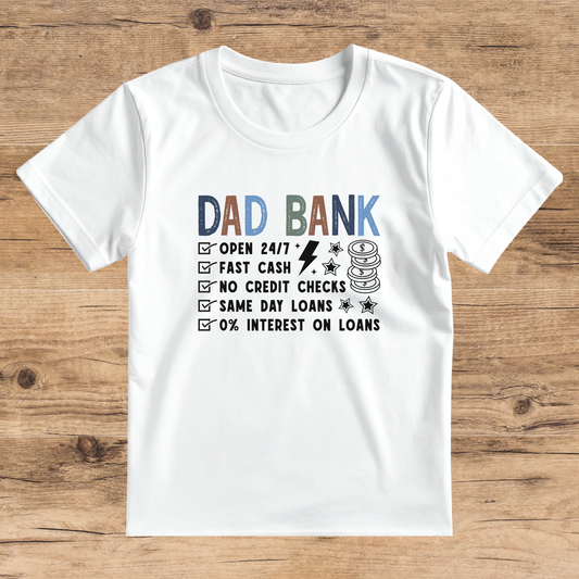 White t-shirt with 'Dad Bank' graphic on a wooden surface