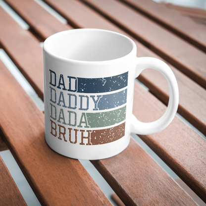 White mug with 'DAD', 'DADDY', 'DADA', 'BRUH' text on a wooden surface
