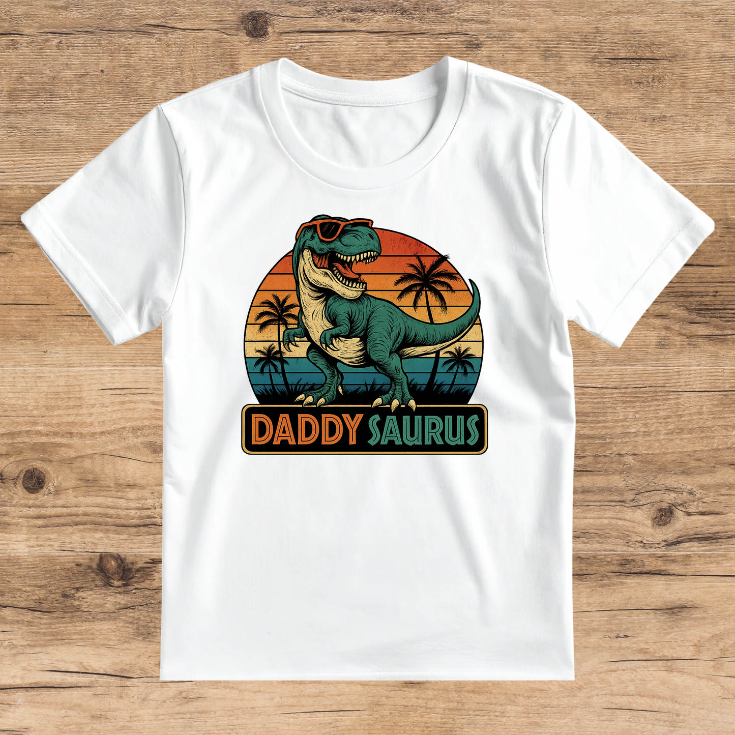 White t-shirt with a dinosaur graphic and 'DADDYSAURUS' text on a wooden surface