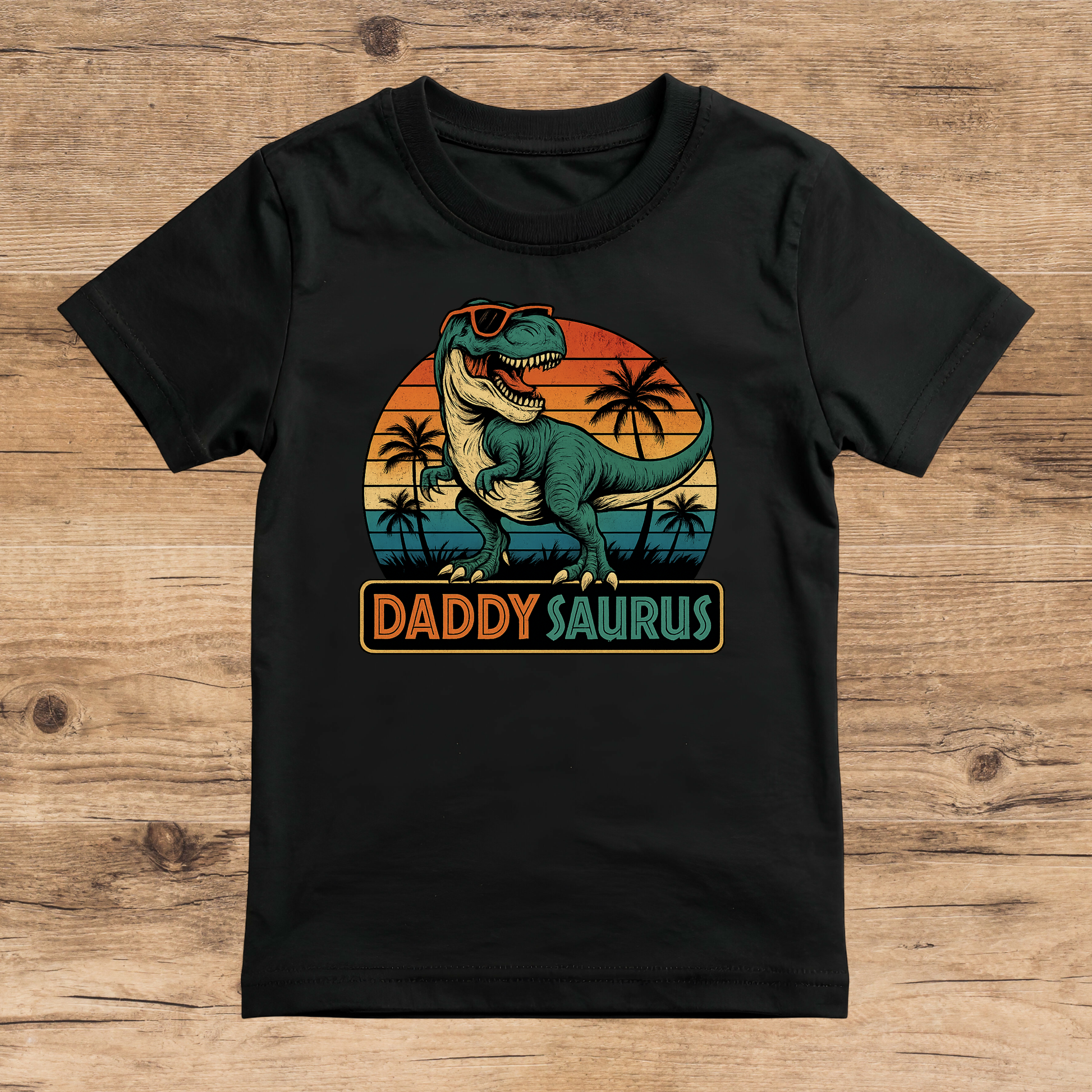 Black t-shirt with 'Daddy Saurus' graphic on a wooden surface
