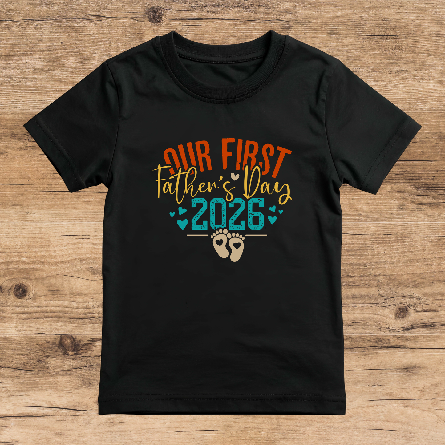 Black t-shirt with 'Our First Father's Day 2026' text on a wooden surface