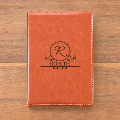 A personalized orange-brown faux-leather notebook cover with a black monogrammed design featuring the letter 'R' in a circle and the name 'ROHITH' below, displayed flat on a wooden surface.