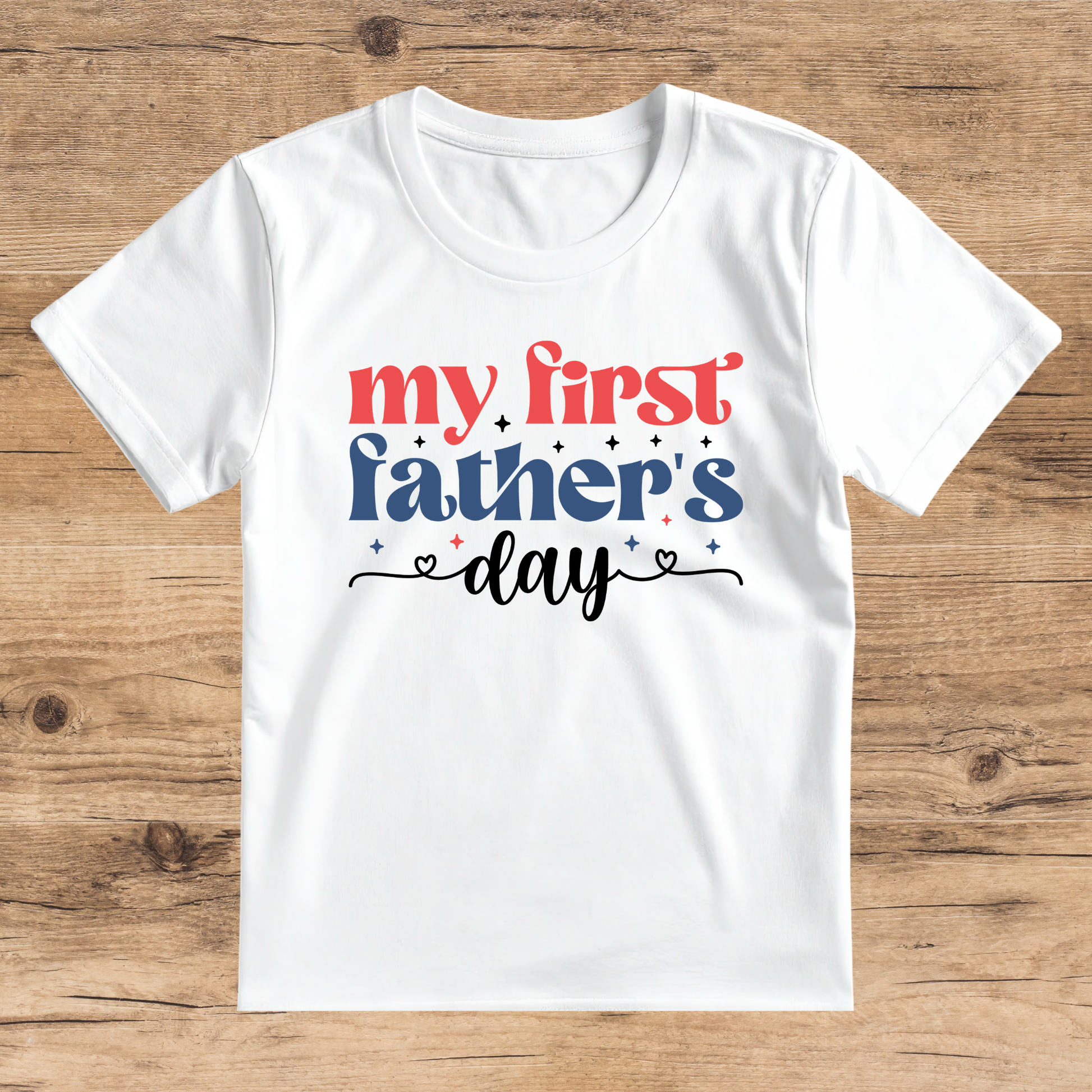 White t-shirt with 'my first father's day' text on a wooden surface