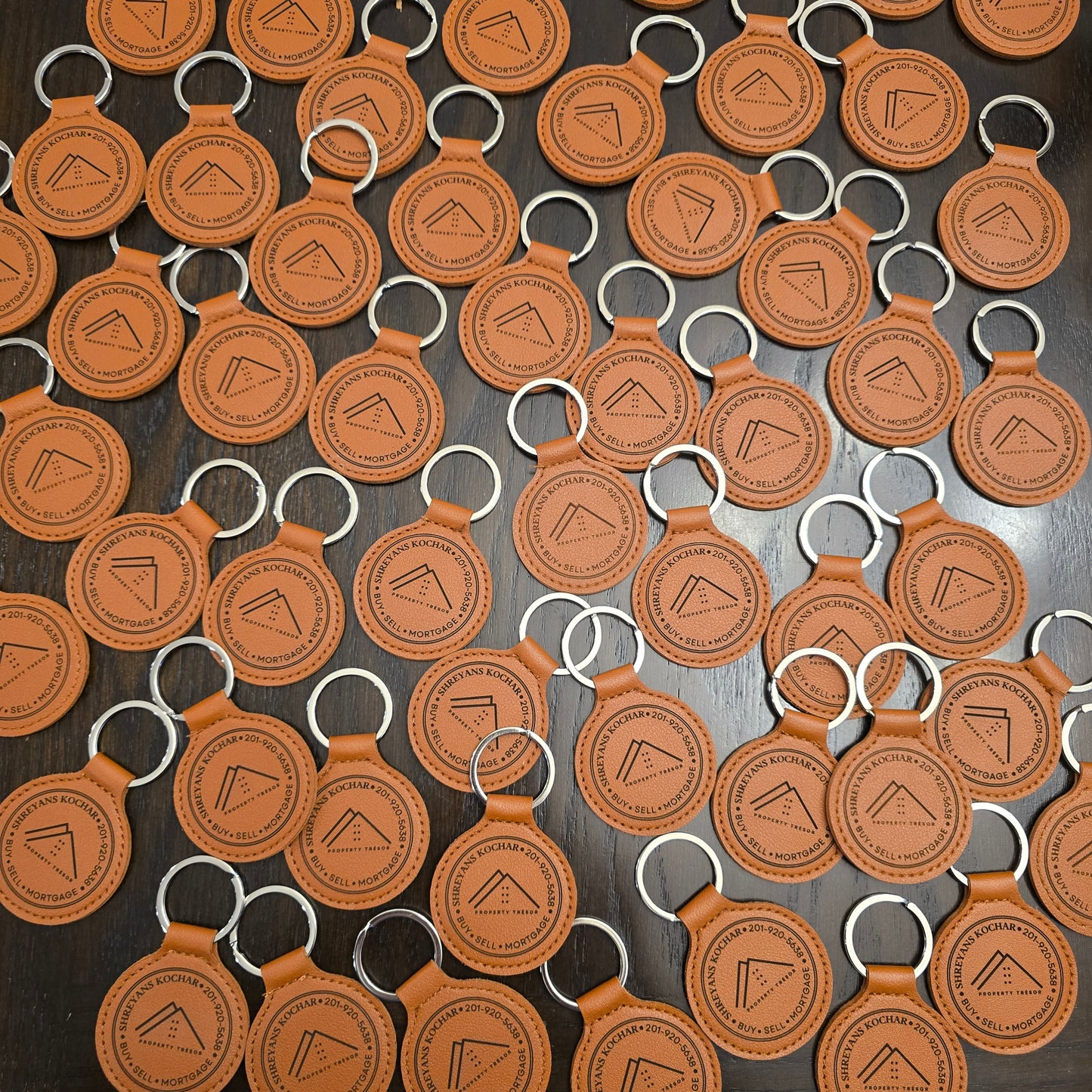 Pattern of brown leather keychains with a logo on a dark surface