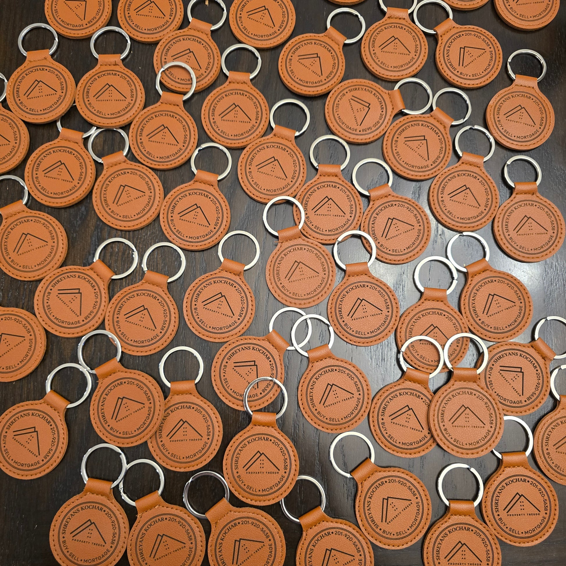 Pattern of brown leather keychains with a logo on a dark surface