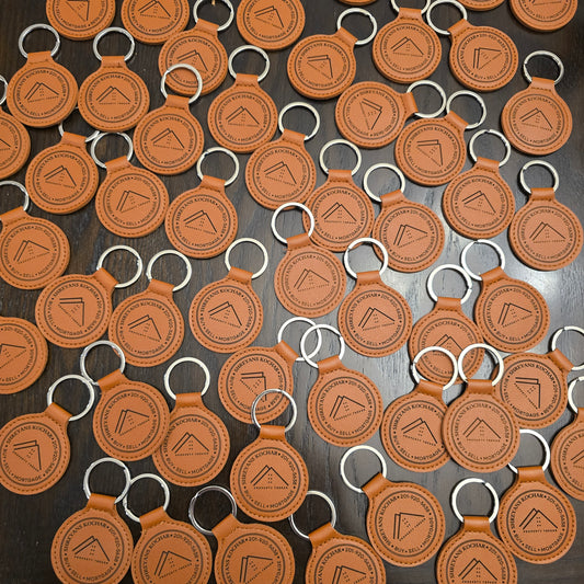 Pattern of brown leather keychains with a logo on a dark surface