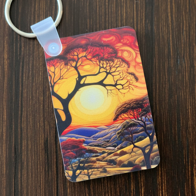Two keychains with artistic designs of a sunset landscape and a architectural structure on a wooden surface.