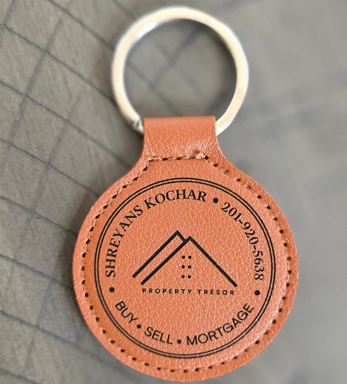 Brown leather keychain with branding on a gray surface