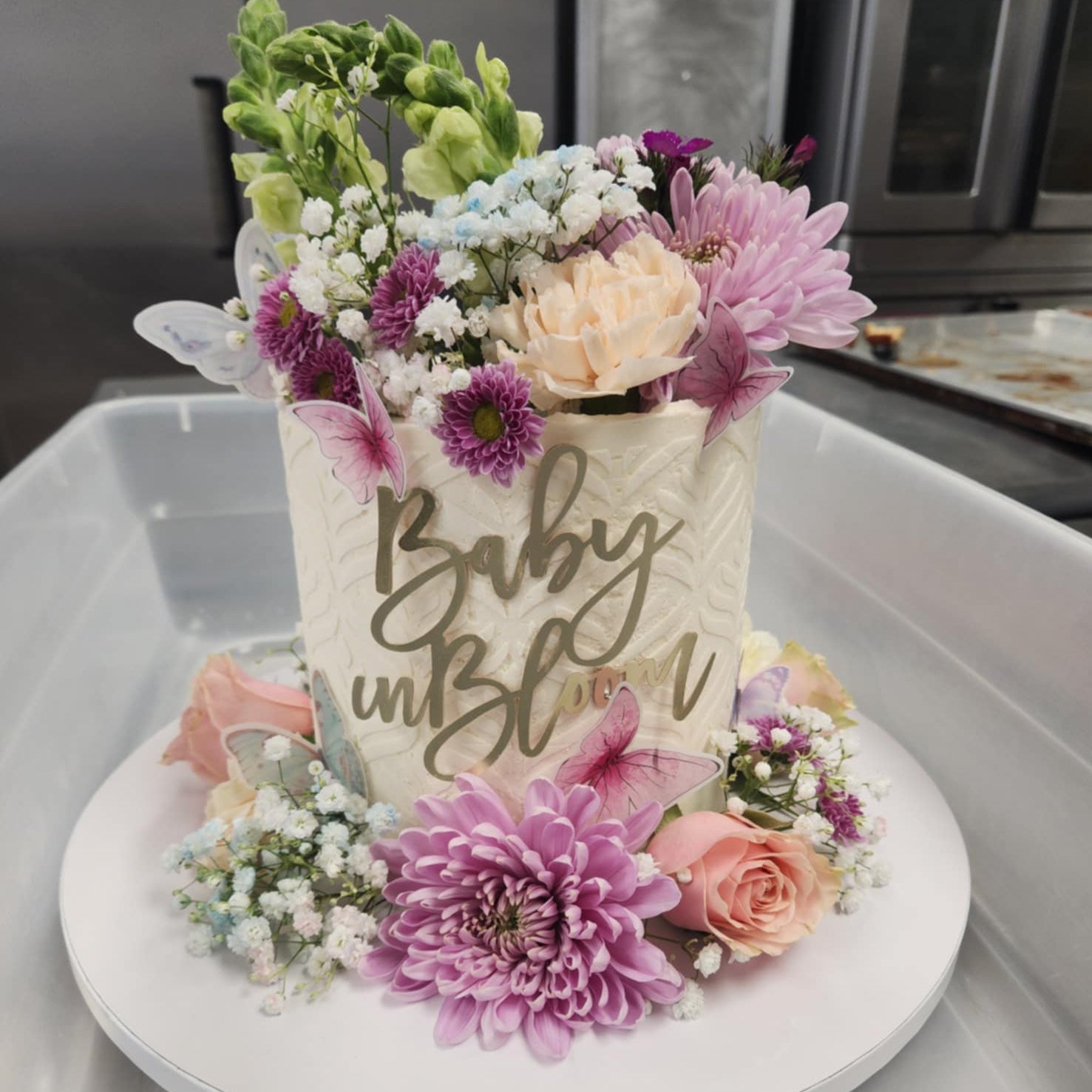 Decorative cake with flowers and 'Baby in Bloom' text on a white surface.