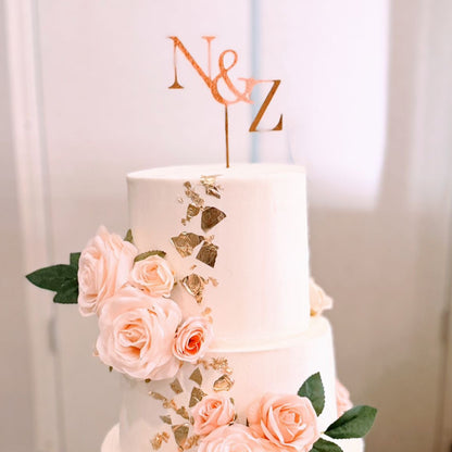 Three-tiered wedding cake with floral decorations and a 'N&Z' topper on a white background.