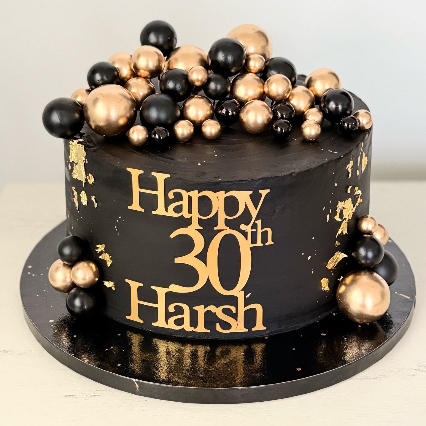 chocolate cake with gold and black decorations and 'Happy 30th Harsh' text on a white background